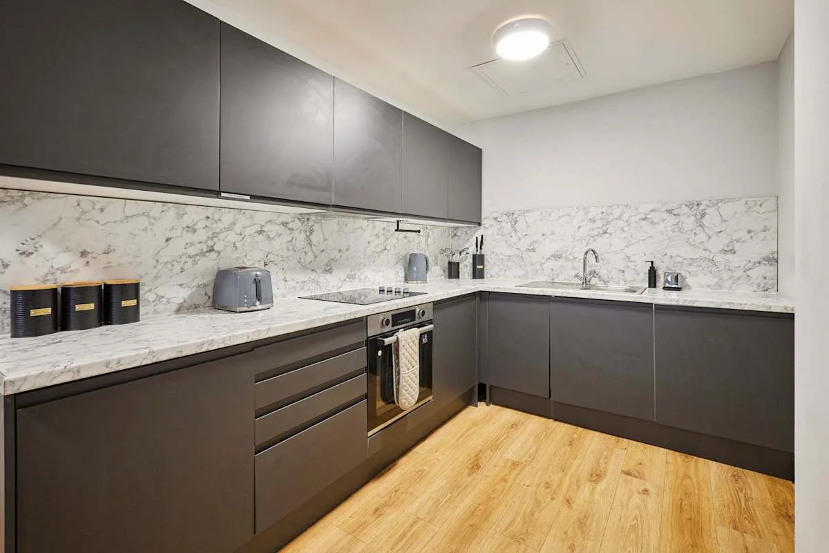 A modern kitchen with dark cabinetry, stone-patterned counters, and wood flooring.