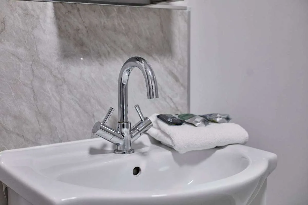A bathroom sink with a curved faucet and folded towels beside it.