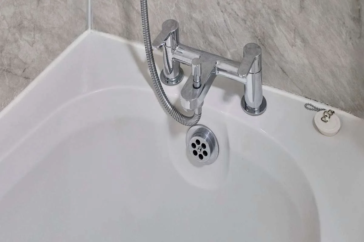 A bathtub with chrome taps and a handheld shower hose.