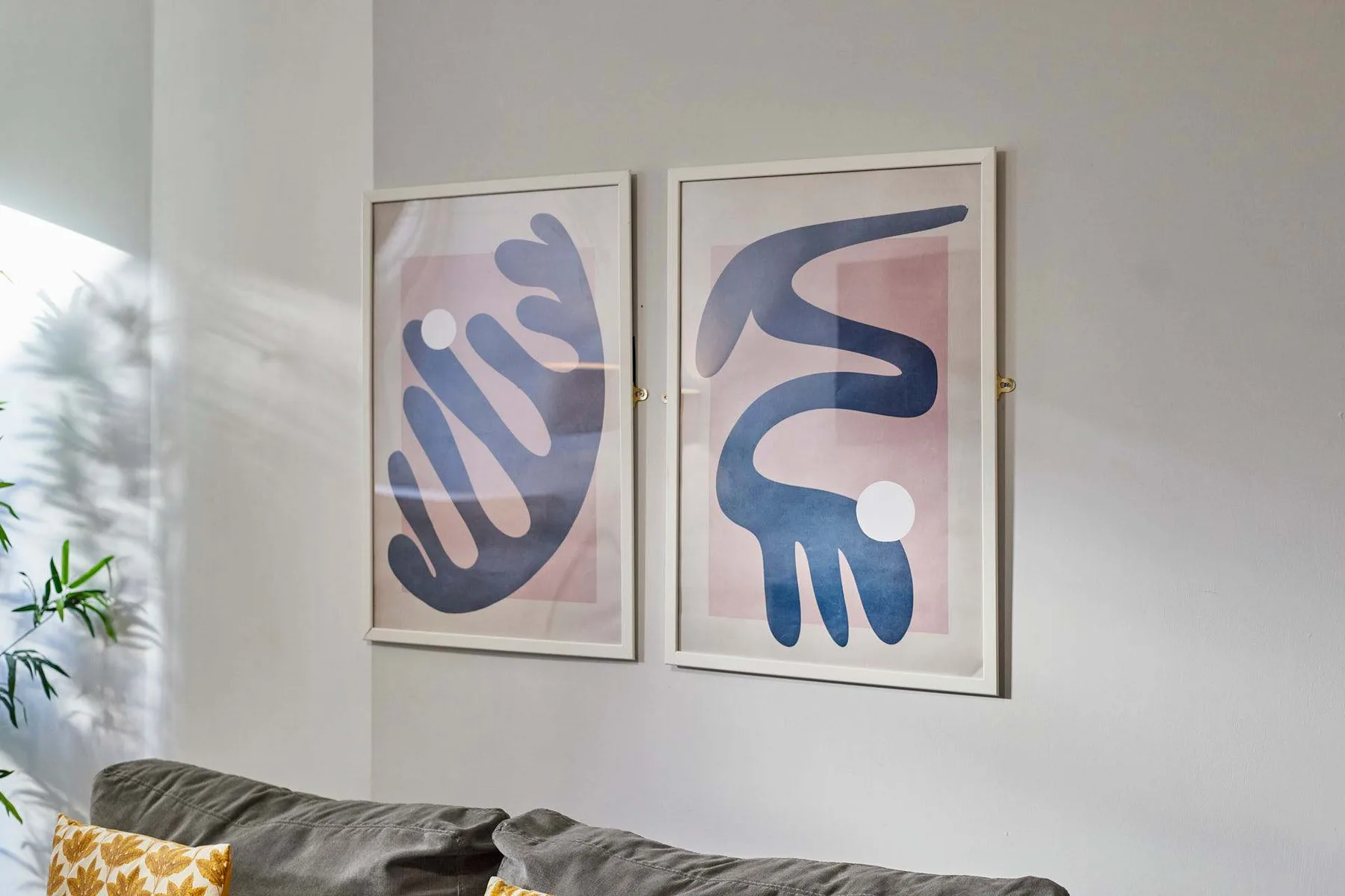 Una sala de estar con un sofá gris bajo dos cuadros abstractos enmarcados.