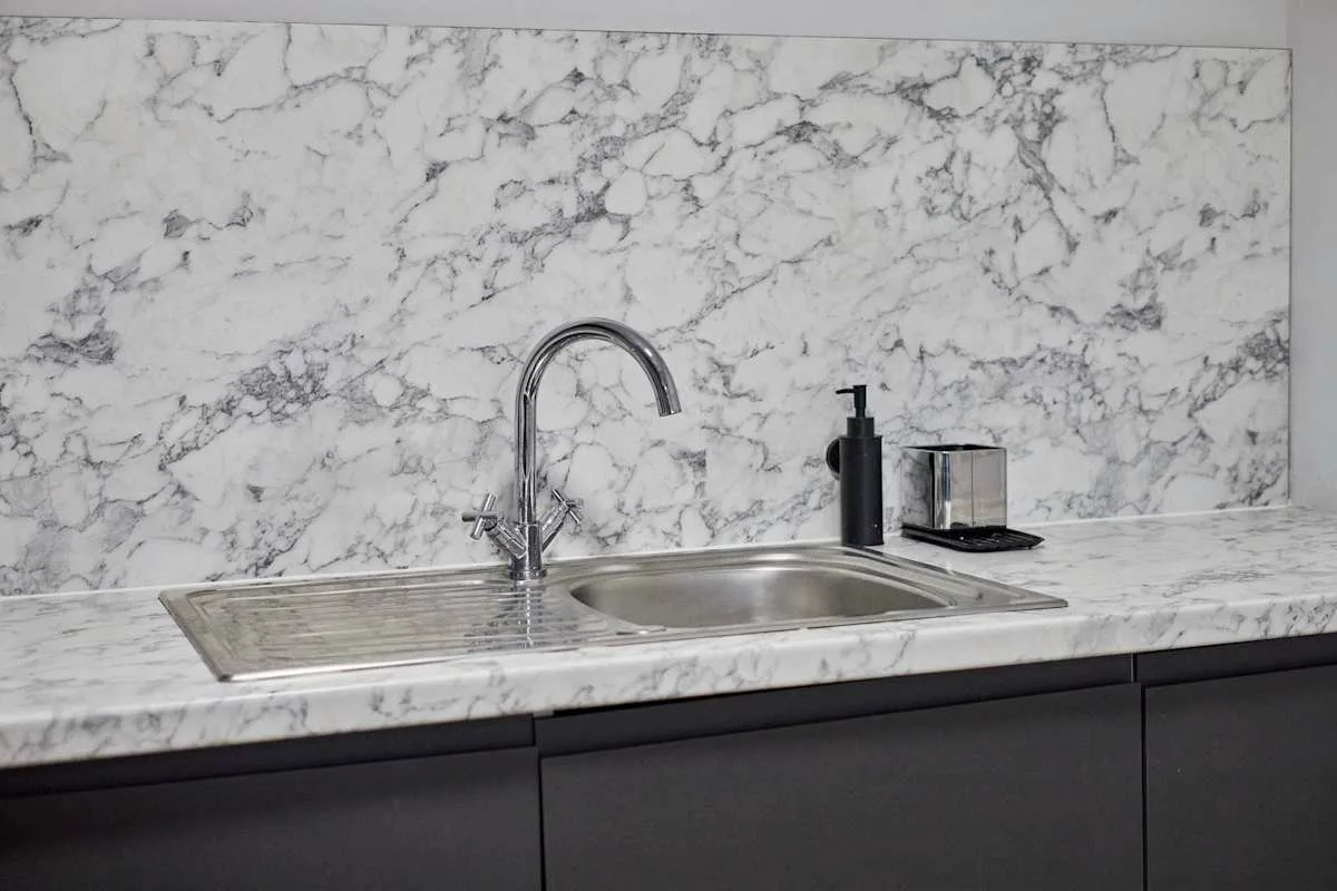 A kitchen counter with a sink and faucet against a veined backsplash.