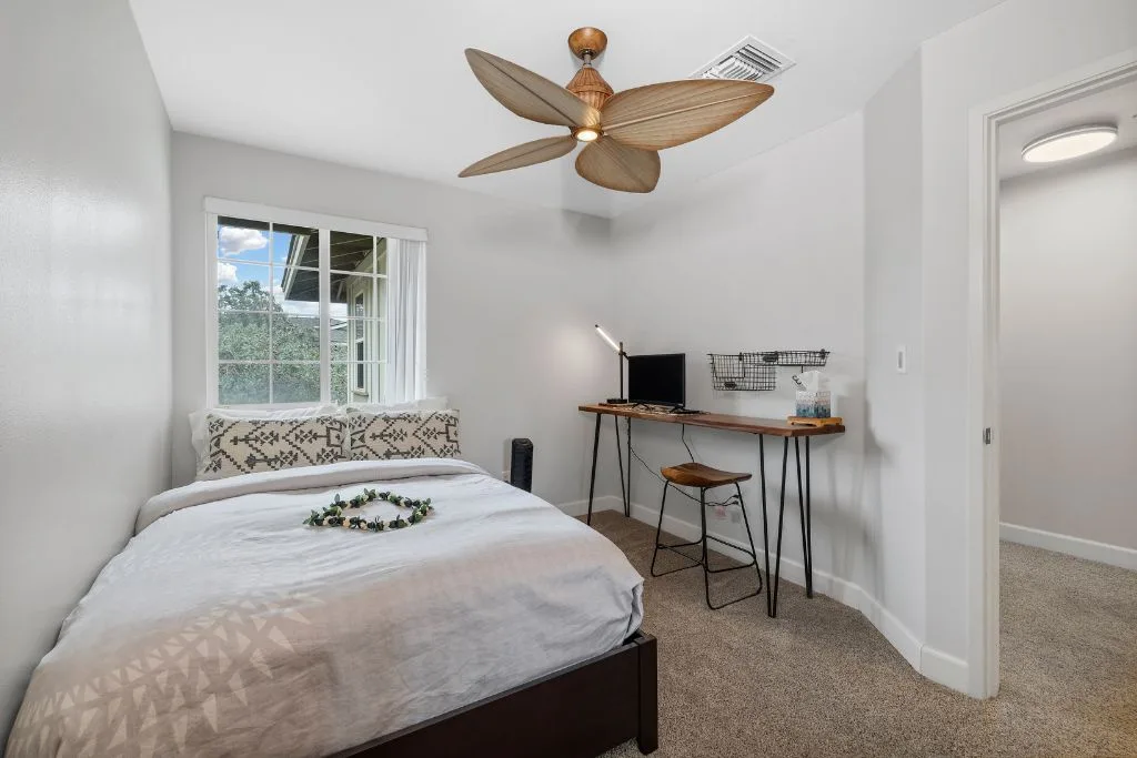 Un dormitorio con una cama junto a una ventana y un escritorio pequeño.