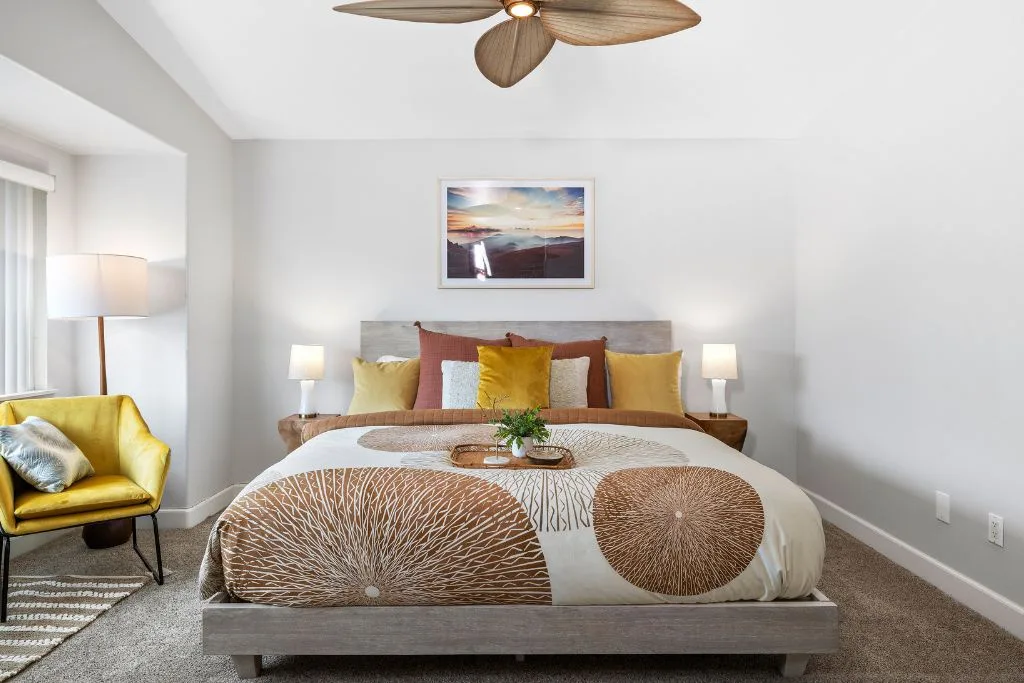 Un dormitorio con una cama, cojines decorativos color mostaza y un cuadro enmarcado encima.