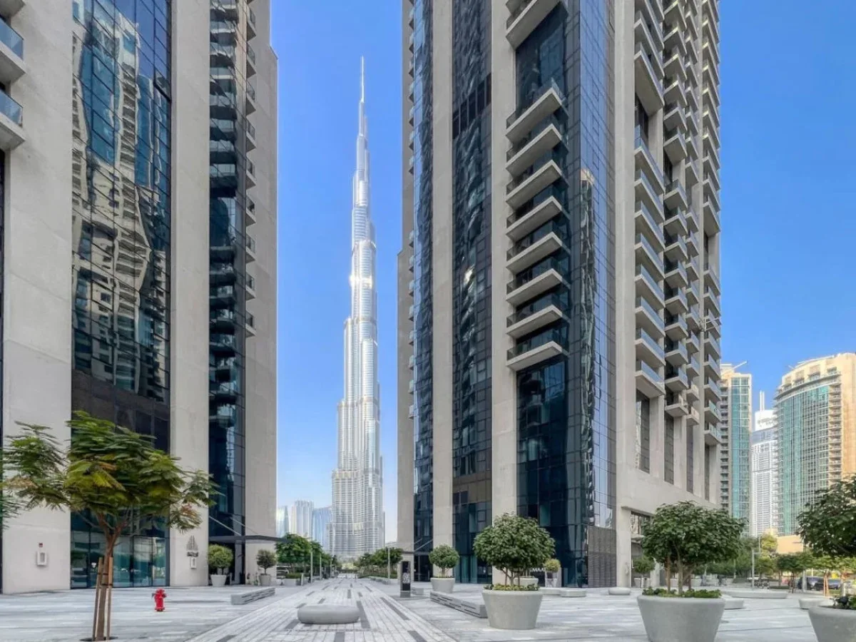 Una plaza urbana entre edificios altos, con un rascacielos esbelto a lo lejos.