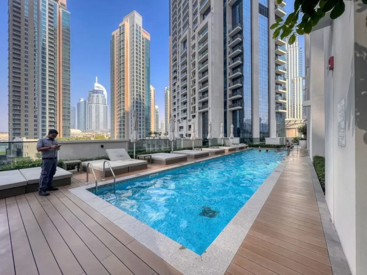 Una piscina en la azotea está rodeada de edificios altos y una terraza de madera.
