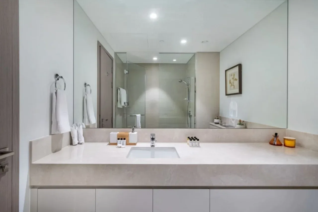 Un tocador de baño luminoso con un espejo amplio y una ducha de vidrio detrás.