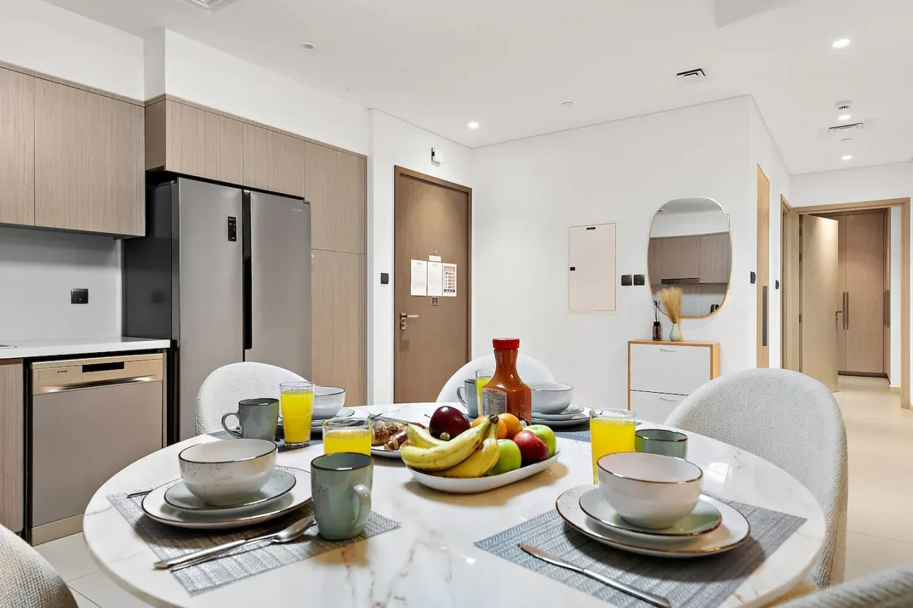 Una mesa puesta con platos y fruta está junto a una cocina con refrigerador.