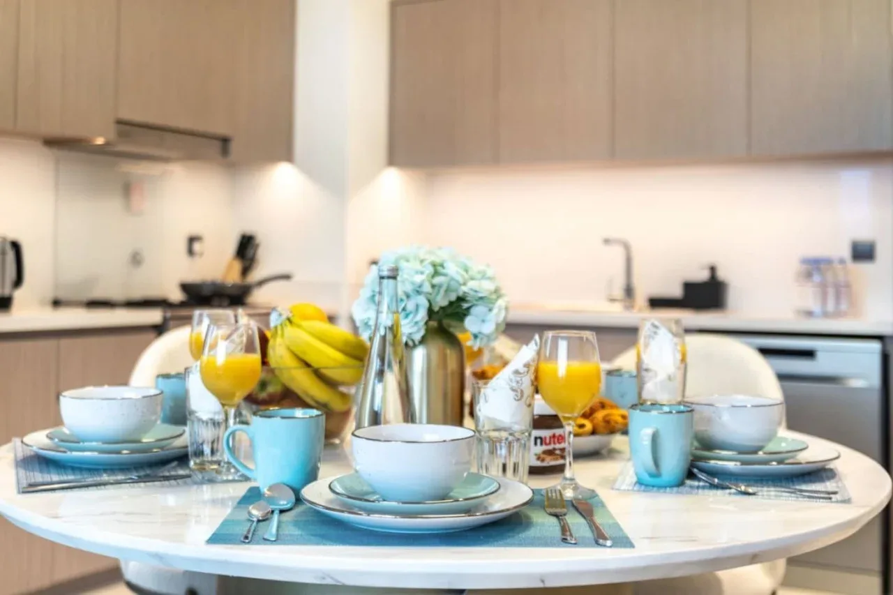 Una mesa de comedor en la cocina está puesta con platos, bebidas, fruta y flores.
