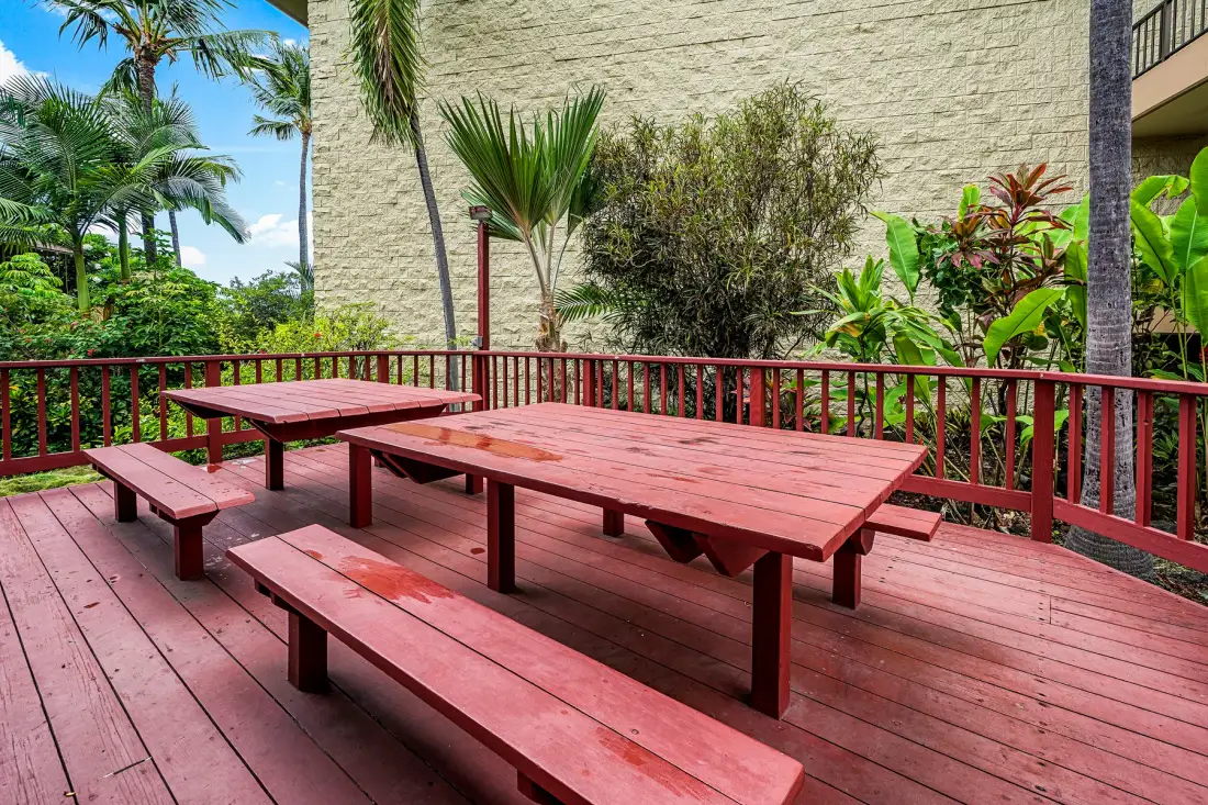 An outdoor wooden deck with picnic tables overlooks a lush garden.