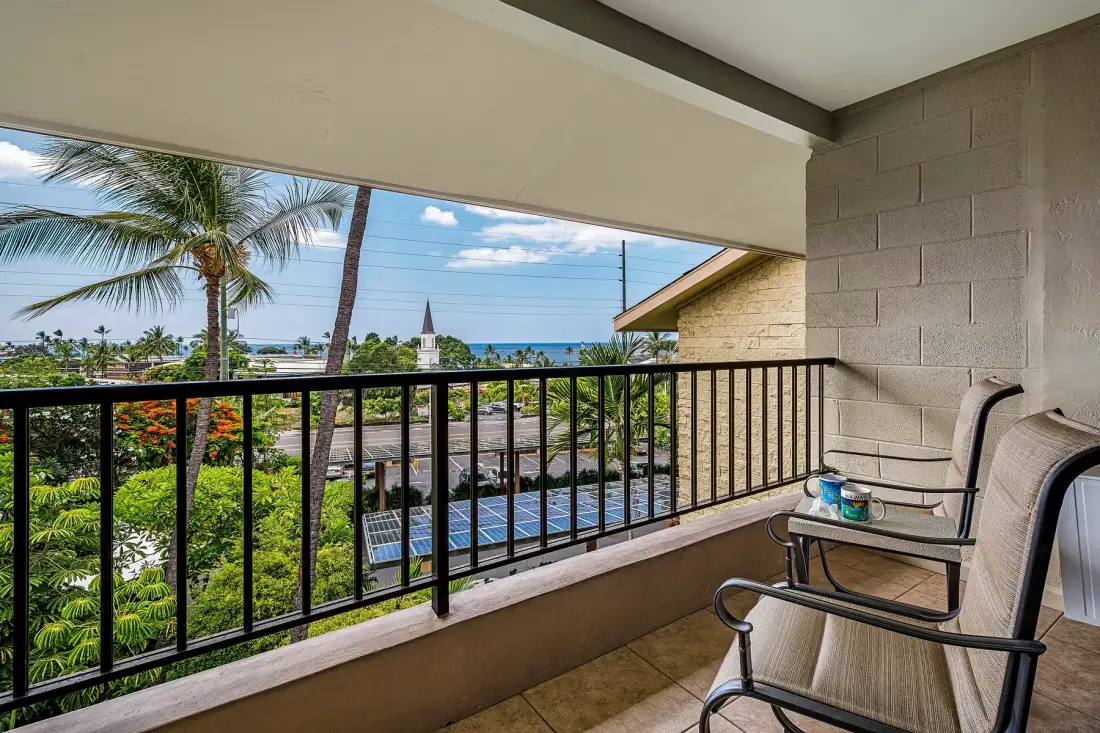 A covered balcony with seating overlooks tropical greenery and the ocean.