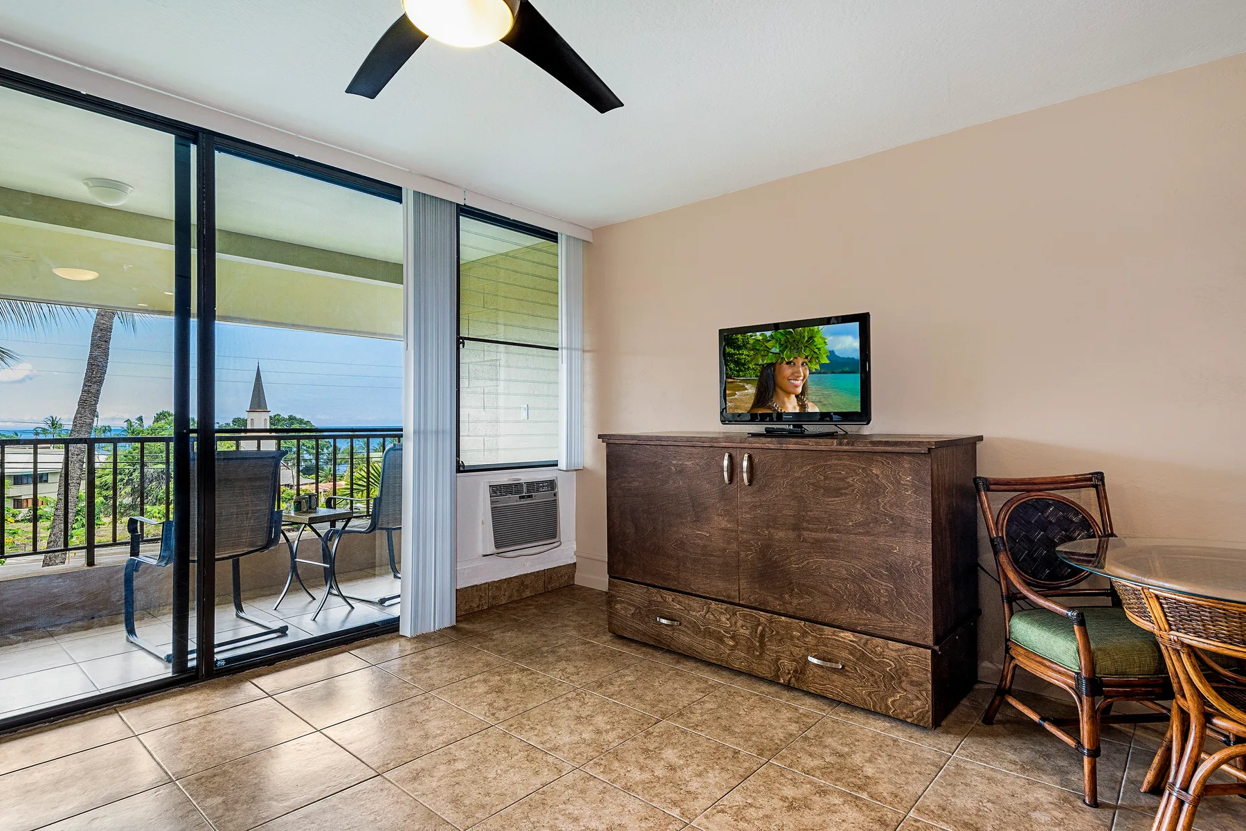 A bedroom seating area with a television, dresser, and sliding glass doors to a balcony.