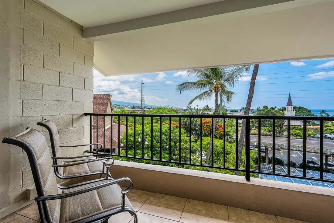 A covered balcony overlooks palm trees, greenery, and the ocean.