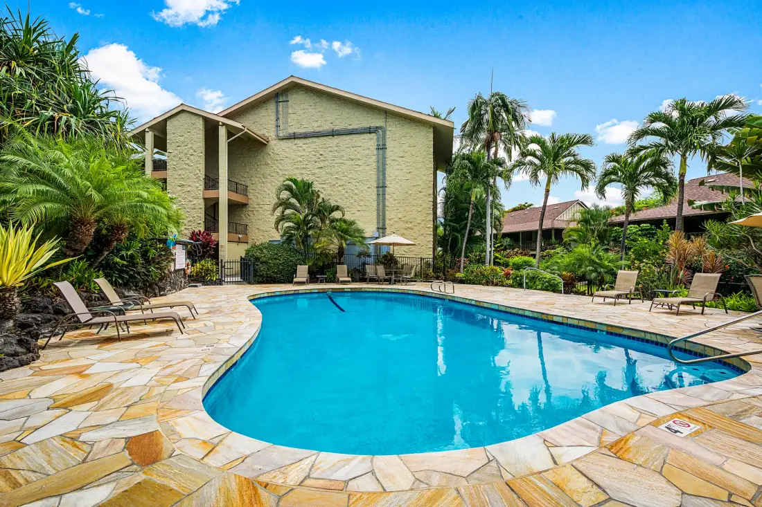 A swimming pool surrounded by a stone-paved deck and tropical landscaping.