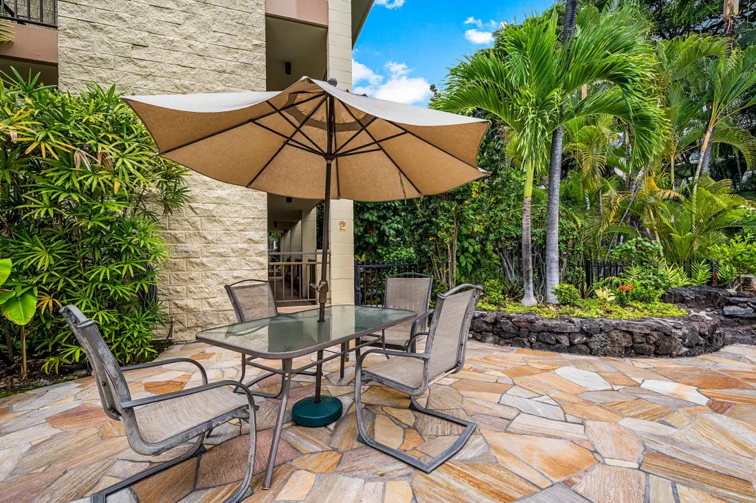 An outdoor patio seating area with a large umbrella and lush tropical plants.