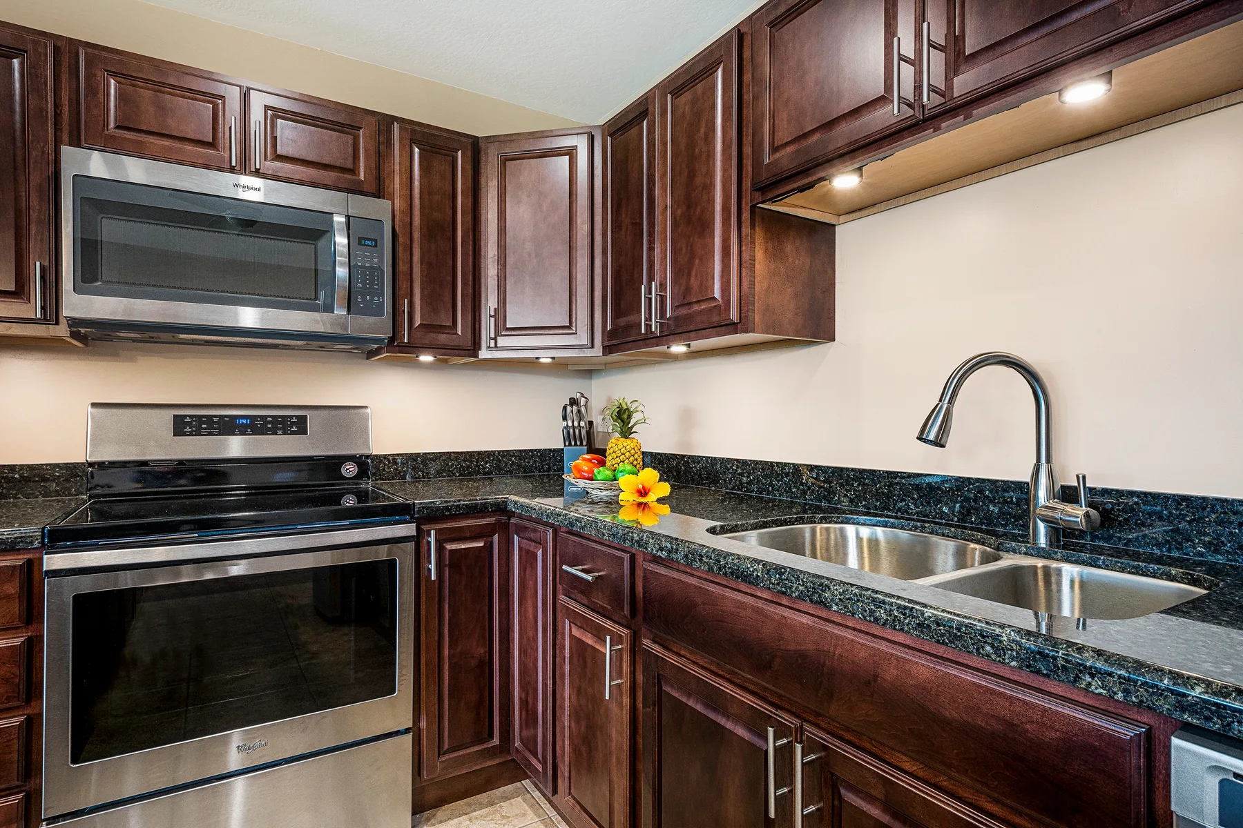 A kitchen with dark wood cabinets, stainless steel appliances, and a double-basin sink.