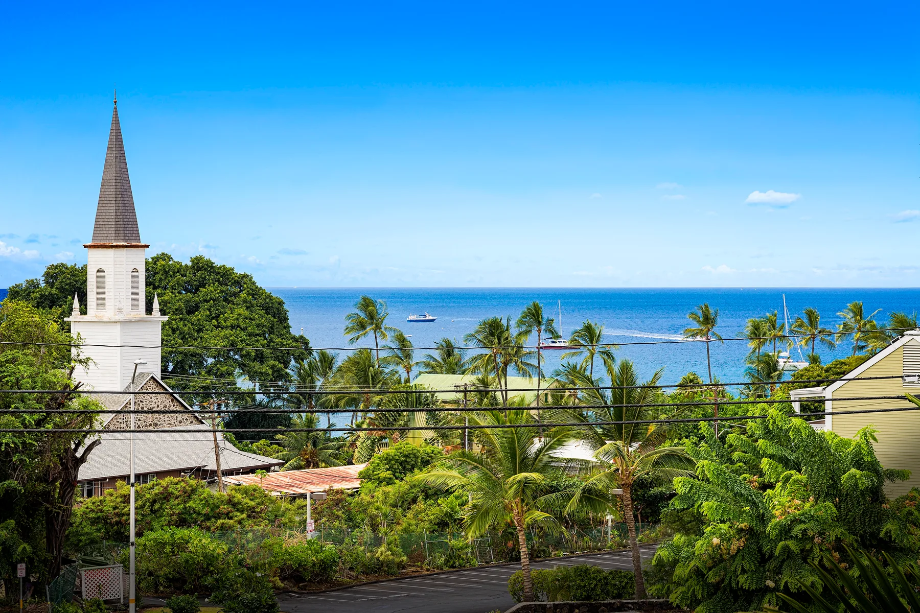A seaside view shows a church steeple, palm trees, and the ocean.