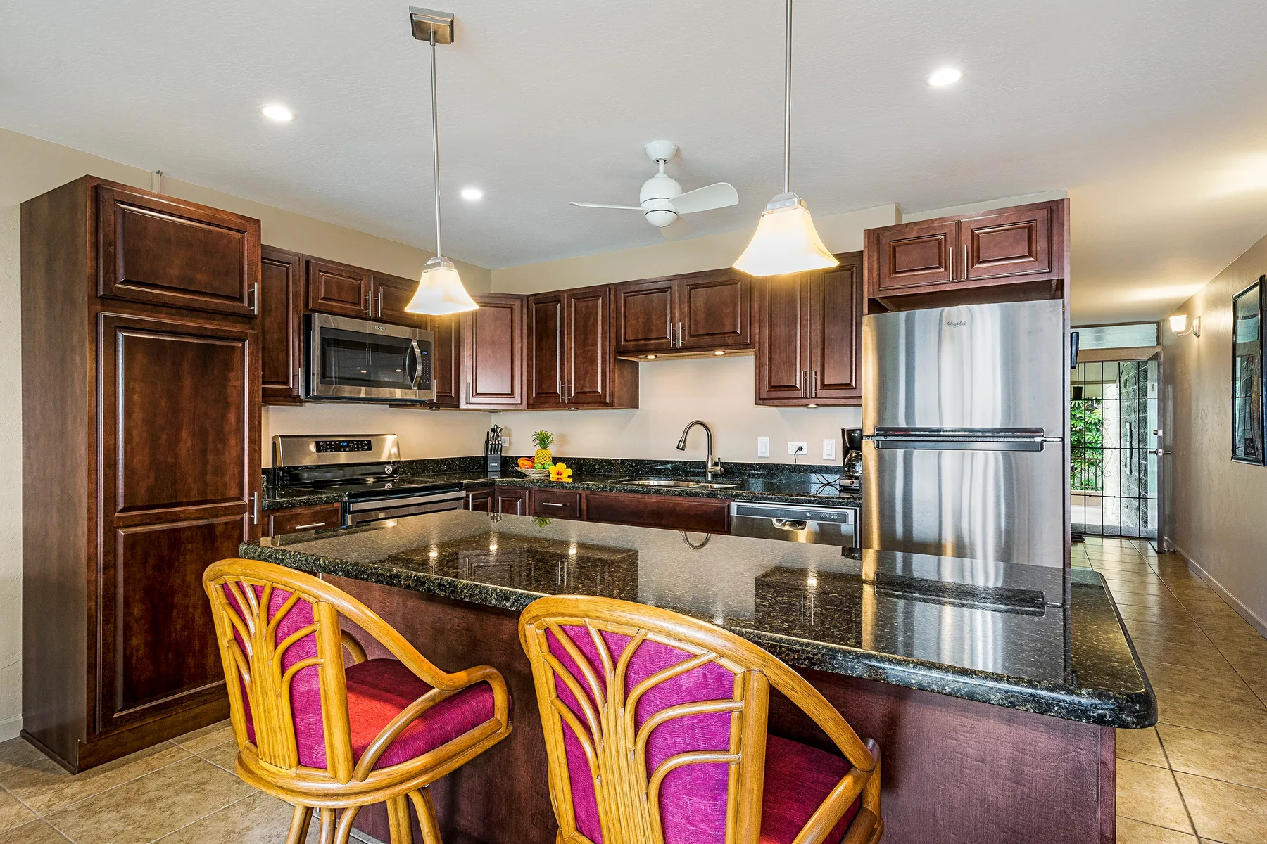 A kitchen with a dark island countertop and colorful bar seating.