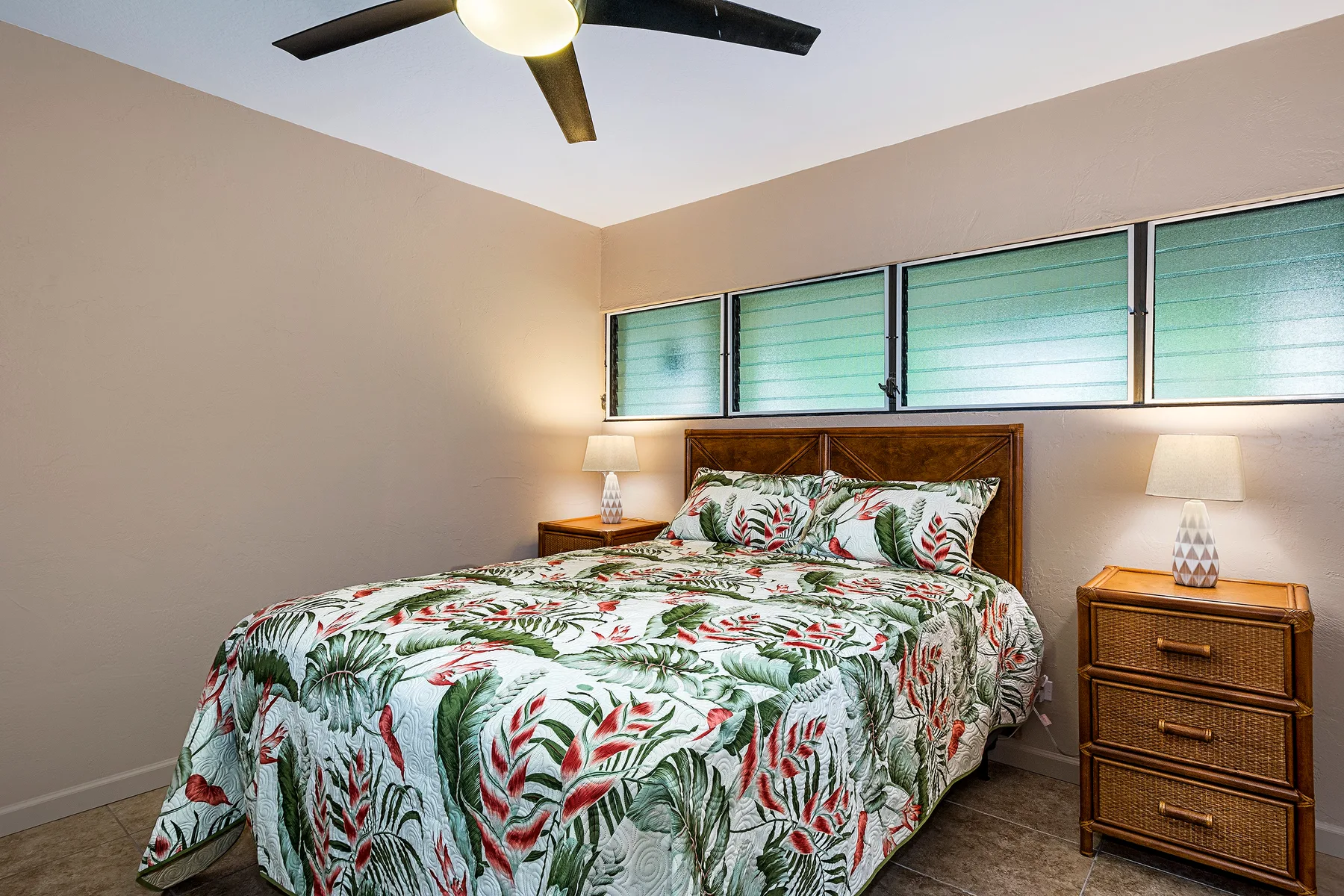 A bedroom with a bed covered in a tropical floral-patterned quilt.