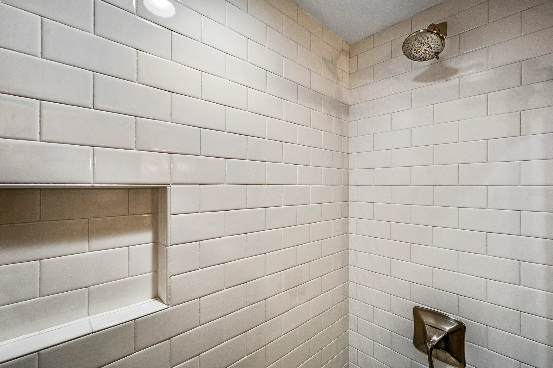 A tiled shower with a recessed wall niche and overhead showerhead.