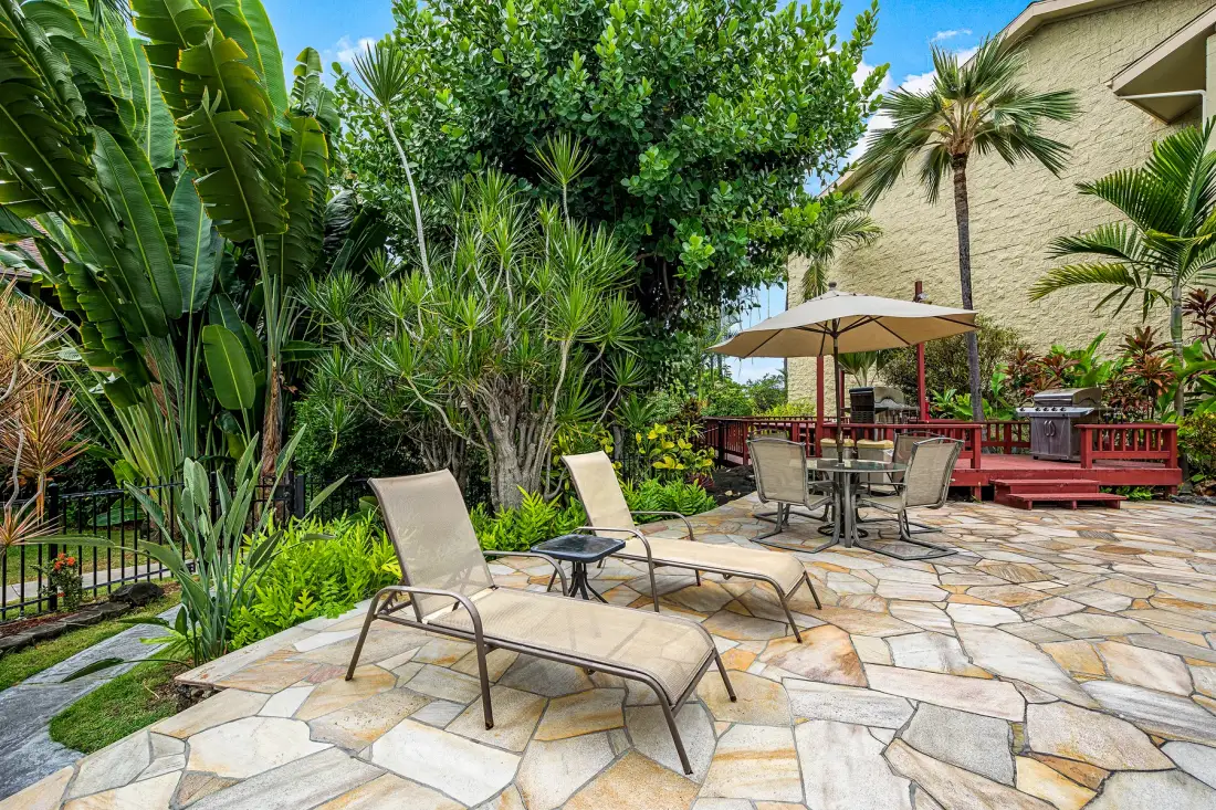 A landscaped patio with lounge seating and a dining table beneath an umbrella.