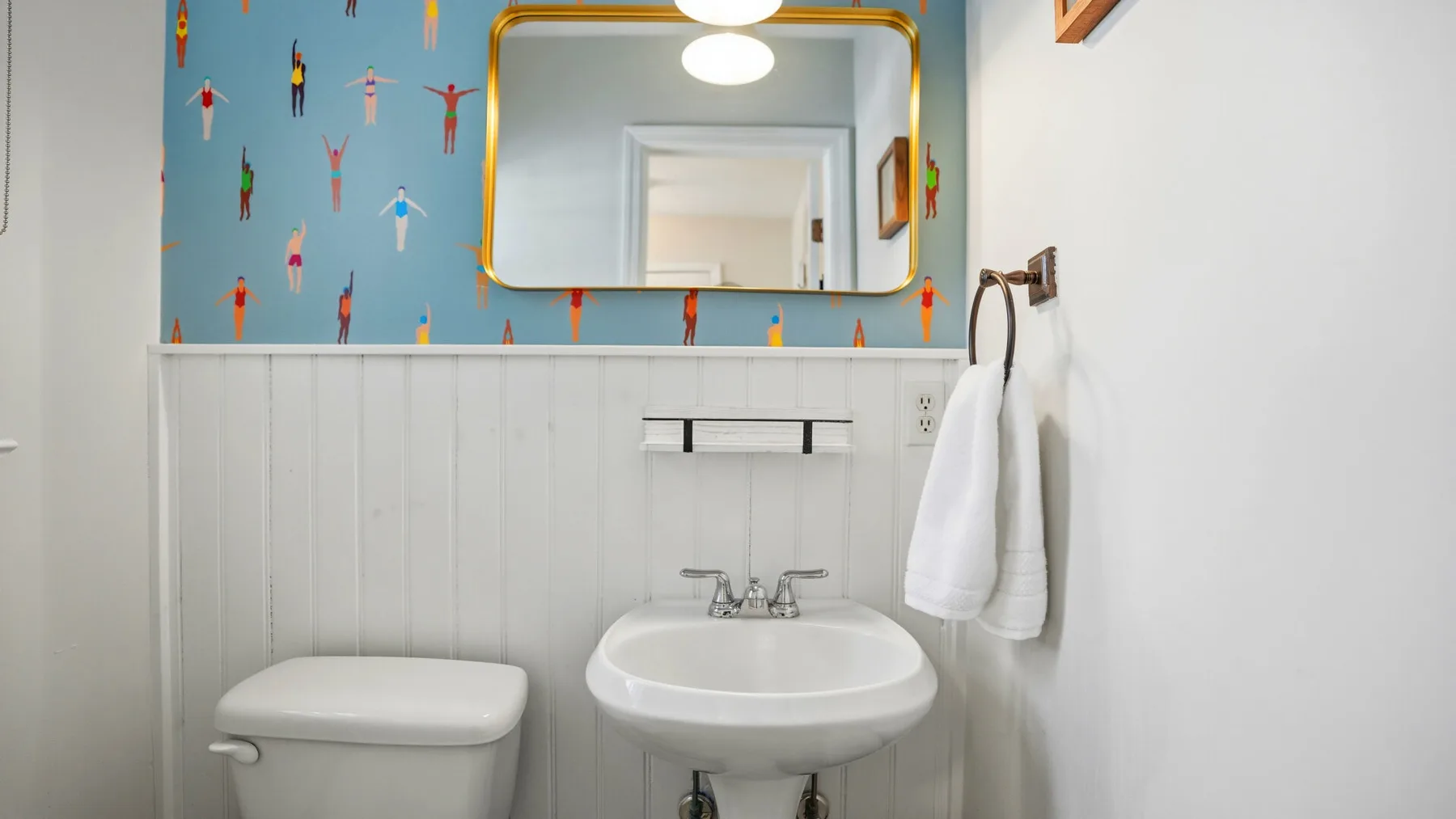 A bathroom with a white sink, mirror, and colorful patterned wall.