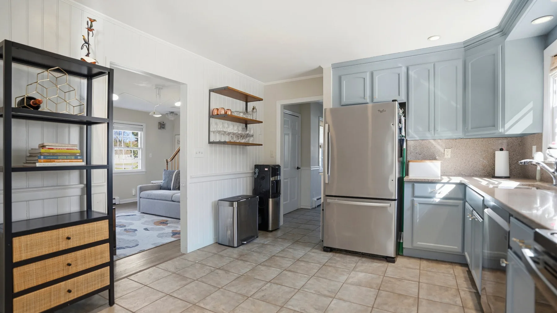 A kitchen with gray cabinets, stainless steel appliances, and an open doorway to a sitting area.