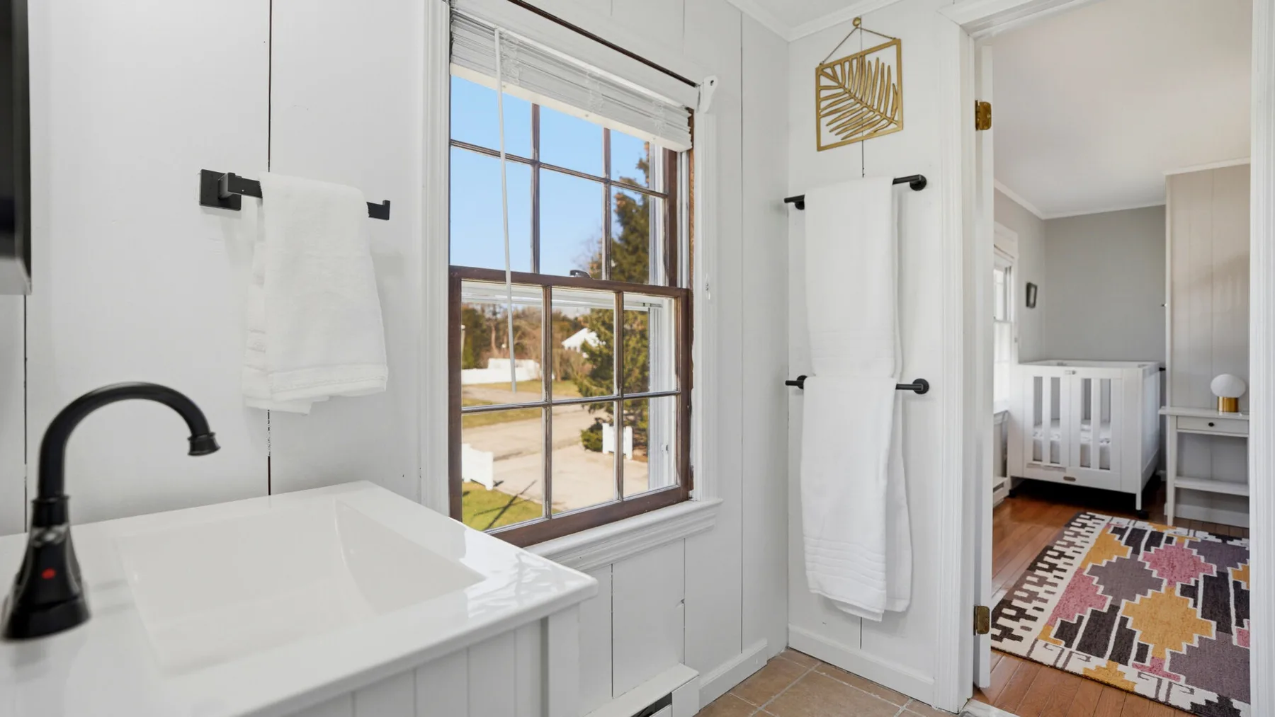 A bright bathroom has a white sink beside a window overlooking the street.