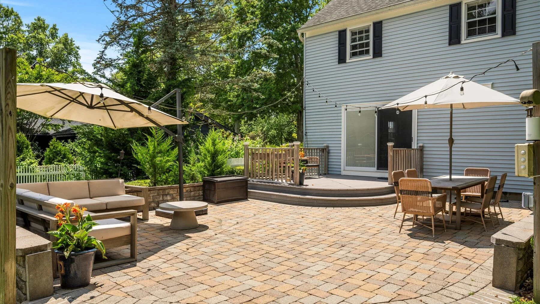An outdoor patio with seating, umbrellas, and a paved surface beside a house.