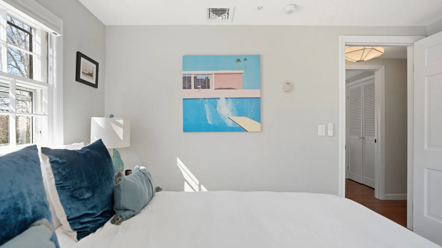 A bedroom with a bed beside a window and a colorful painting on the wall.