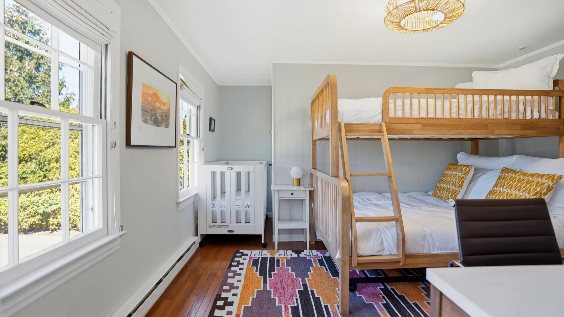 A bright bedroom with wooden bunk beds, a crib, and a colorful rug.
