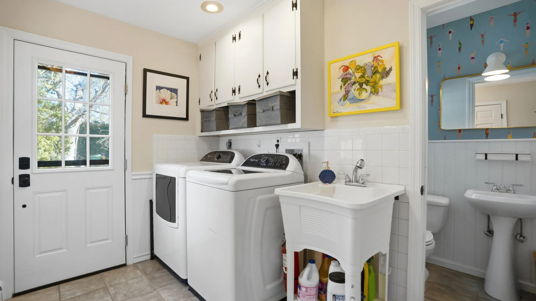 A laundry room with washing machines beside a utility sink and an open bathroom doorway.