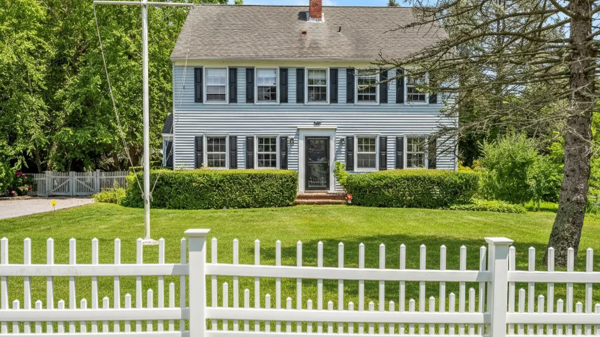 A two-story house with a front lawn and white picket fence.