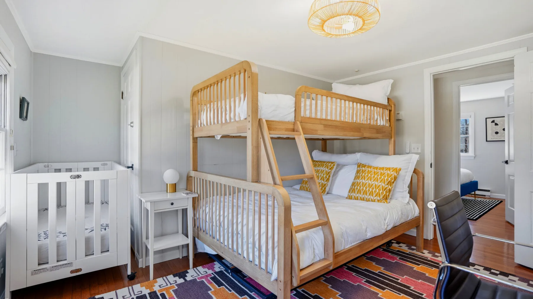 A bright bedroom with wooden bunk beds and a white crib.
