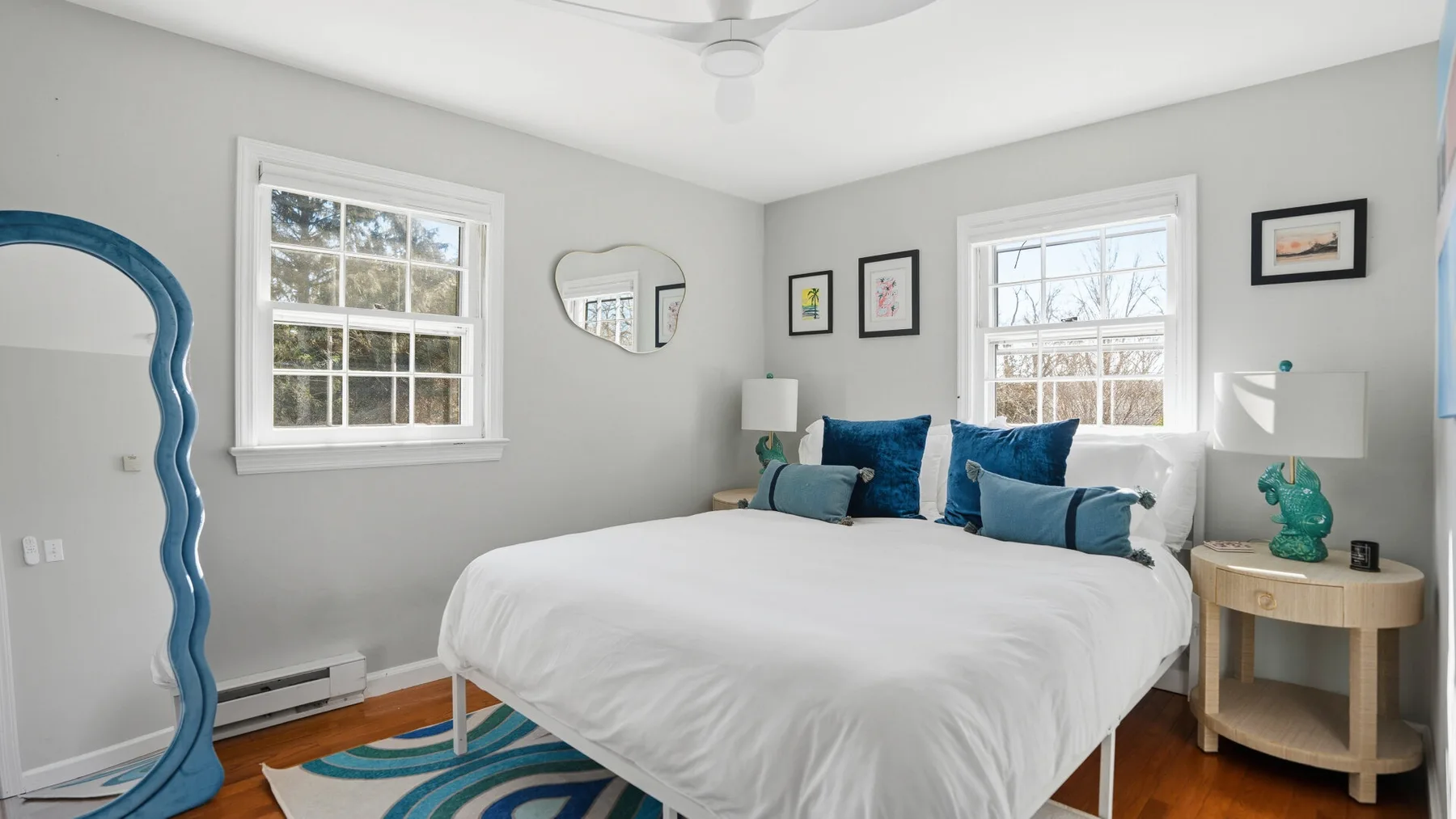 A bright bedroom with a white bed, blue pillows, and windows.