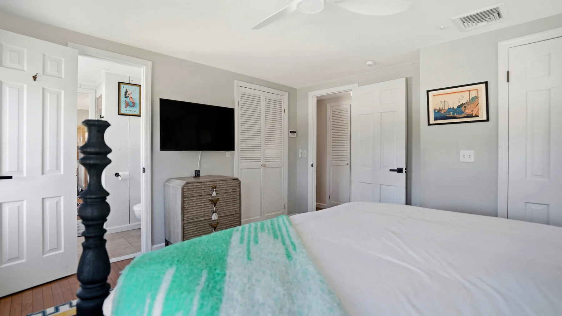 A bright bedroom with a bed, a television, and framed artwork on the walls.