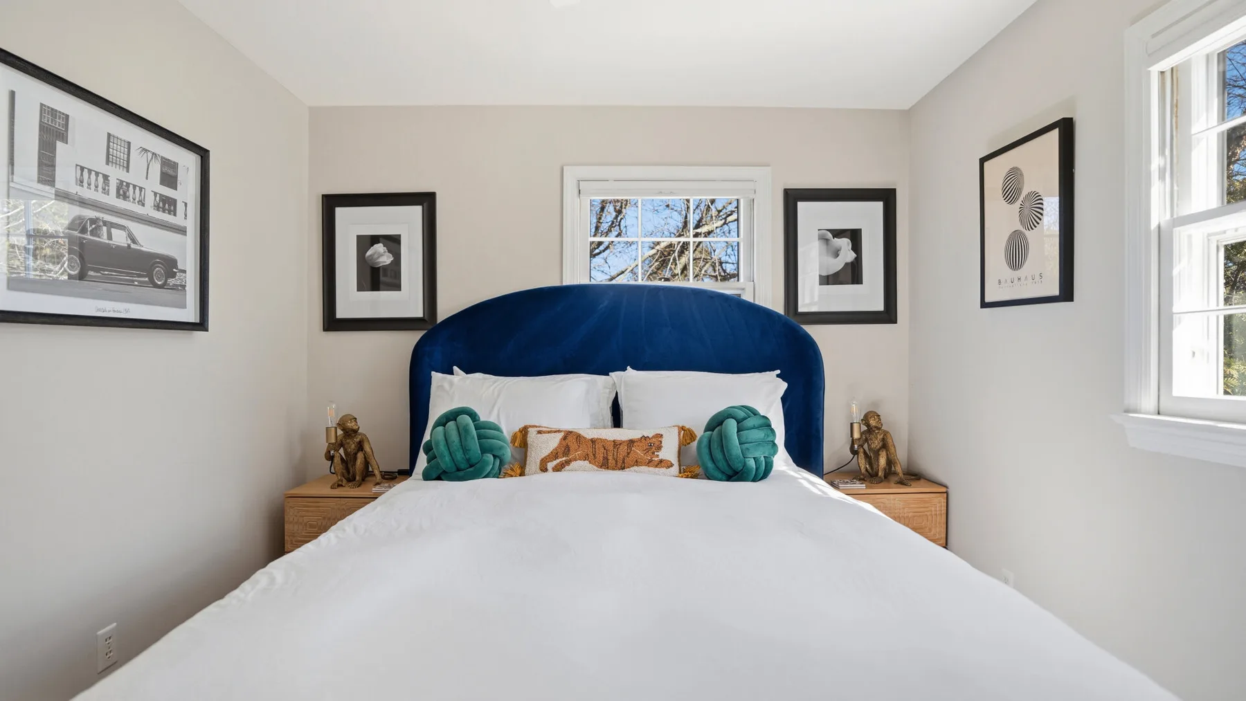 A bedroom with a bed beneath a blue upholstered headboard and framed wall art.