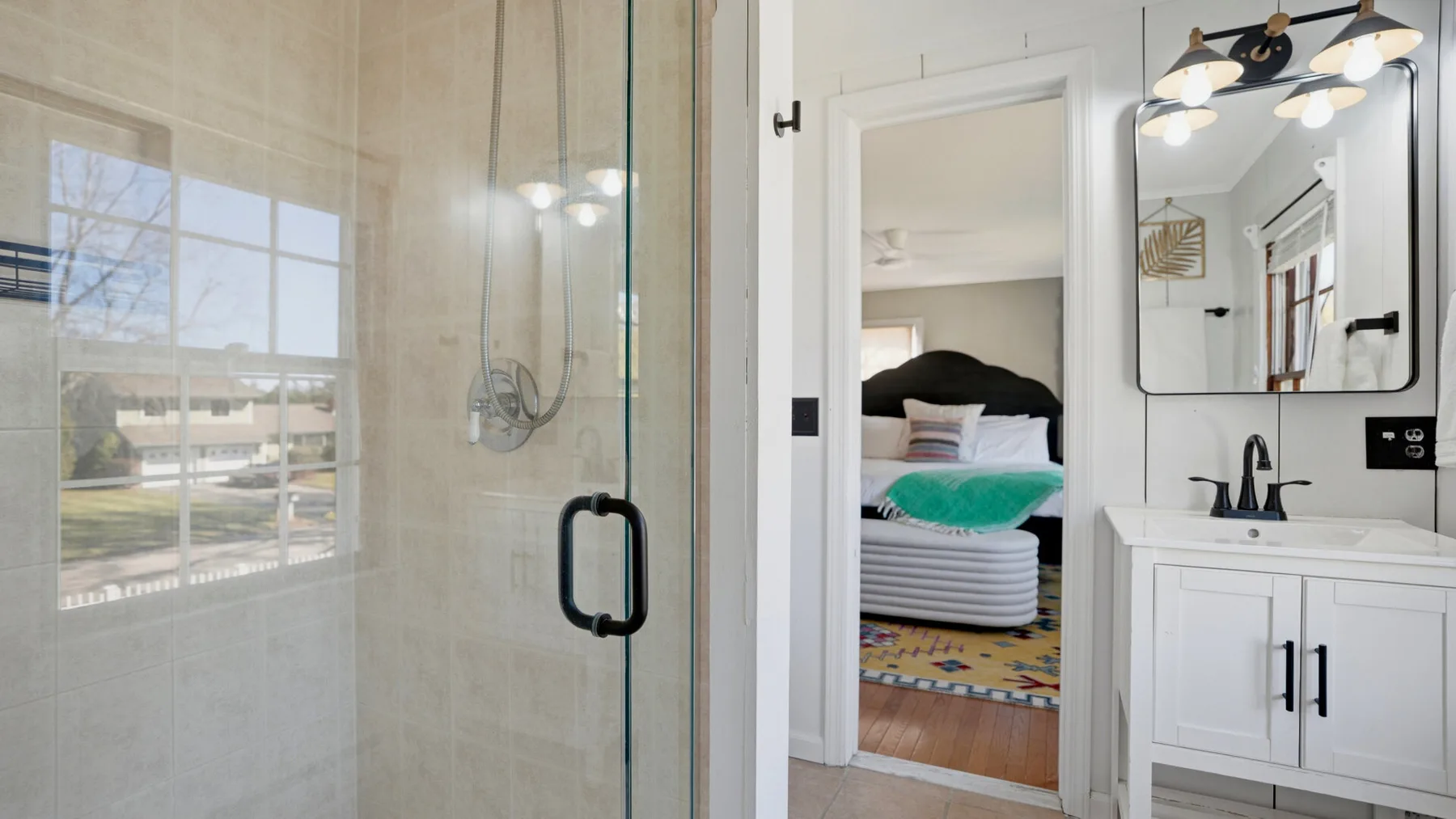 A bathroom with a glass shower and a white vanity beside an open doorway.