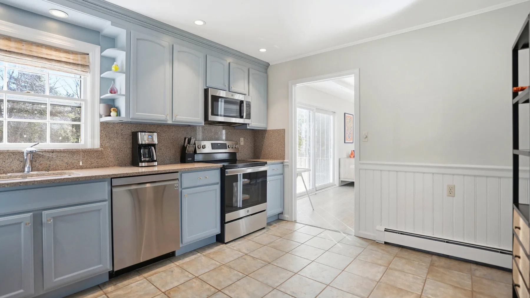 A bright kitchen with blue cabinetry, stainless steel appliances, and a tiled floor.