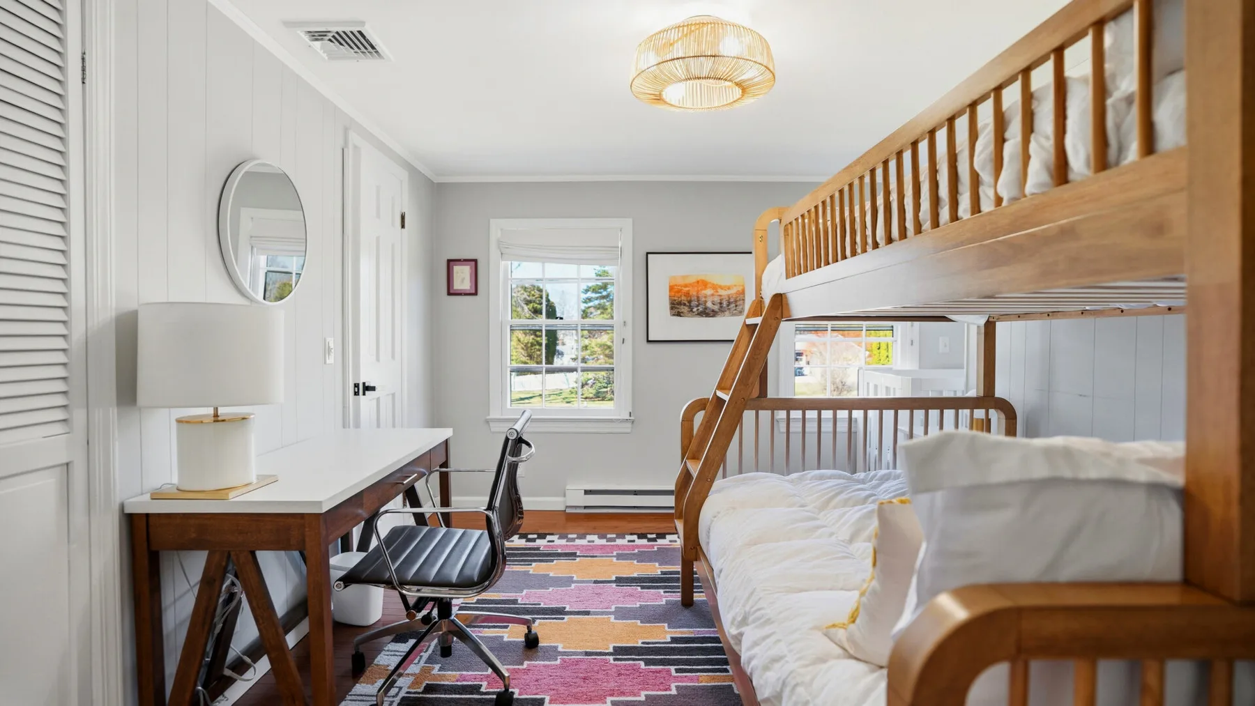 A bright bedroom with a wooden bunk bed, desk, and colorful rug.