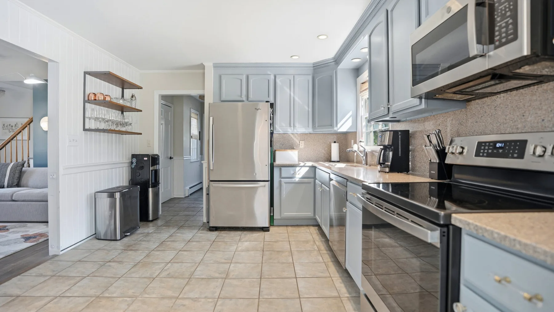 A bright kitchen with gray cabinets, stainless steel appliances, and tiled flooring.