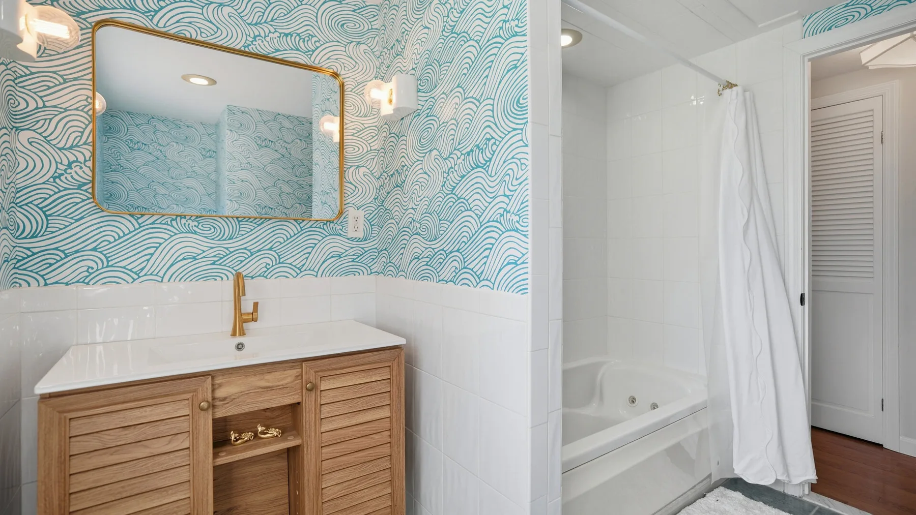 A bathroom vanity with a mirror stands beside a bathtub and shower curtain.