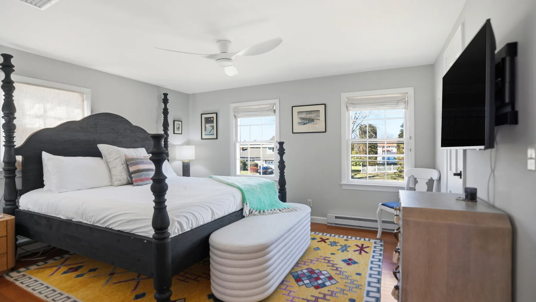 A bedroom with a dark bed, pale bedding, and a colorful rug.