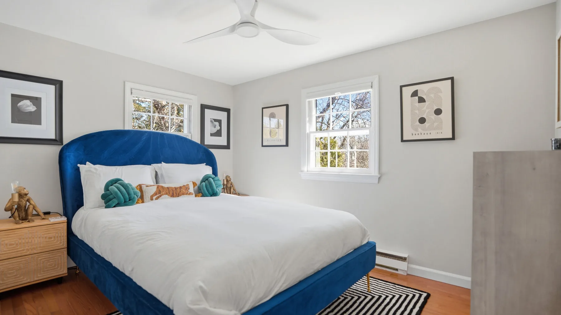 A bedroom with a blue bed, white bedding, and framed artwork on the walls.