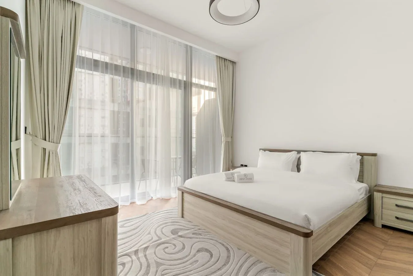 Un dormitorio luminoso con una cama grande y cortinas transparentes en las ventanas.