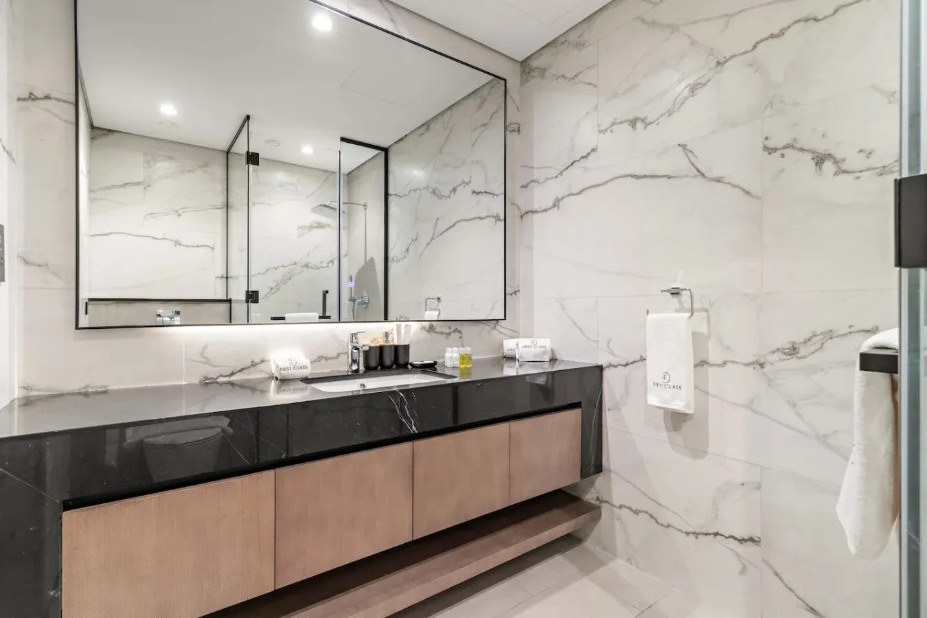 Un tocador de baño moderno con un espejo amplio y paredes con vetas de mármol.