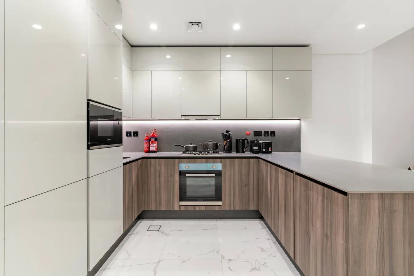 Una cocina moderna con gabinetes claros, muebles inferiores en tono madera y una estufa.