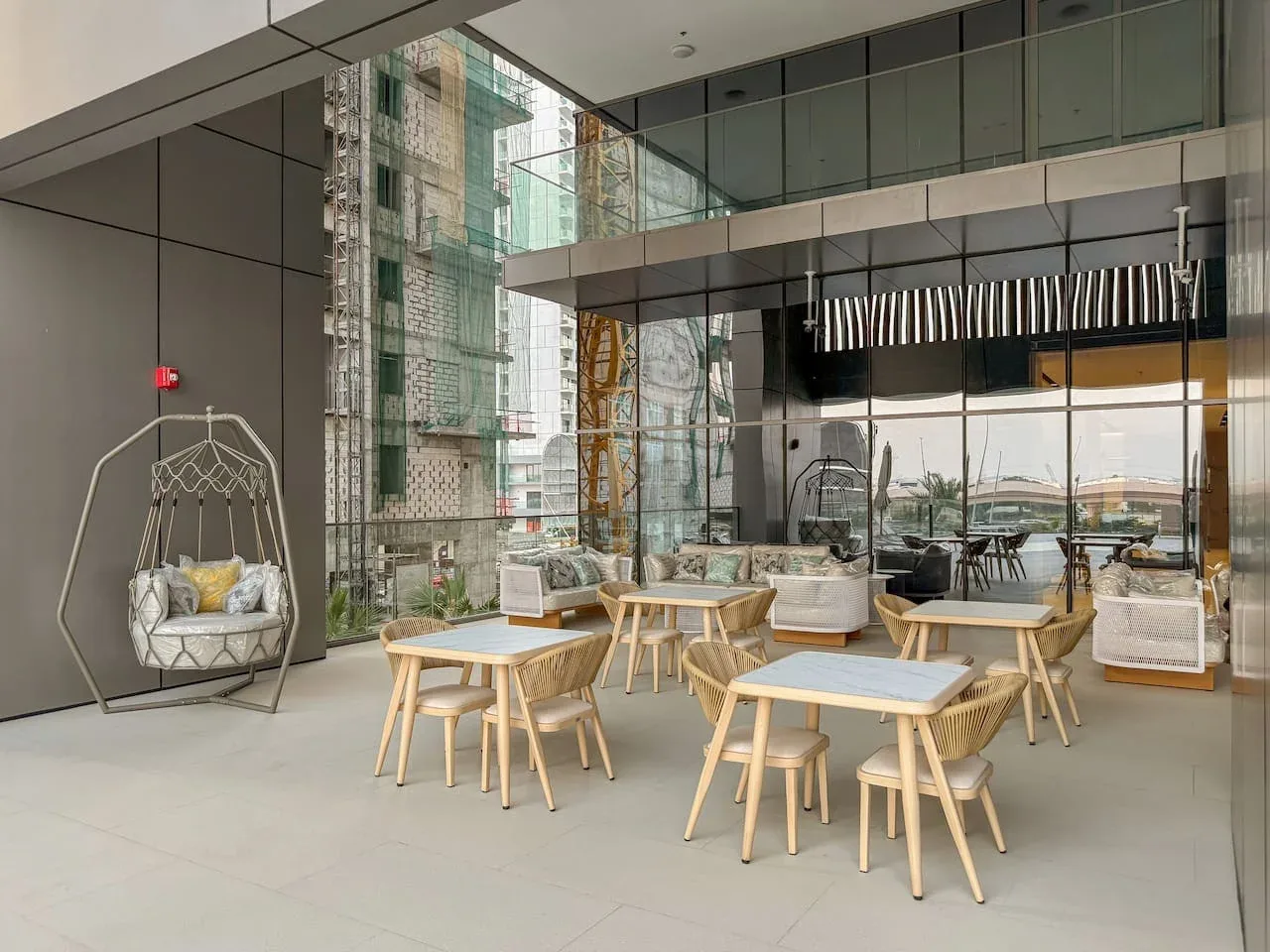 Una sala interior moderna con mesas y asientos junto a grandes ventanales.