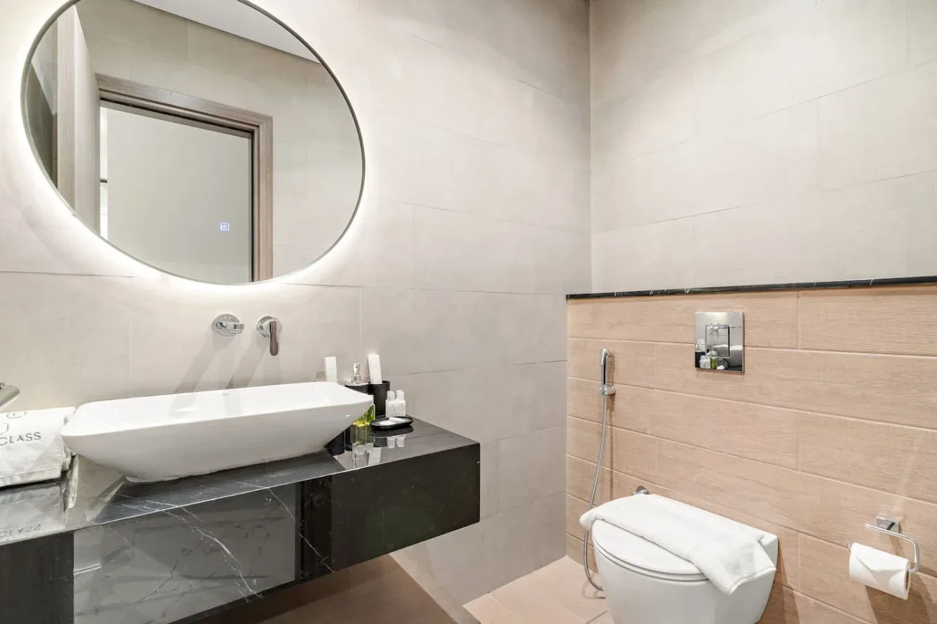 Un baño moderno con lavabo suspendido, espejo ovalado e inodoro.