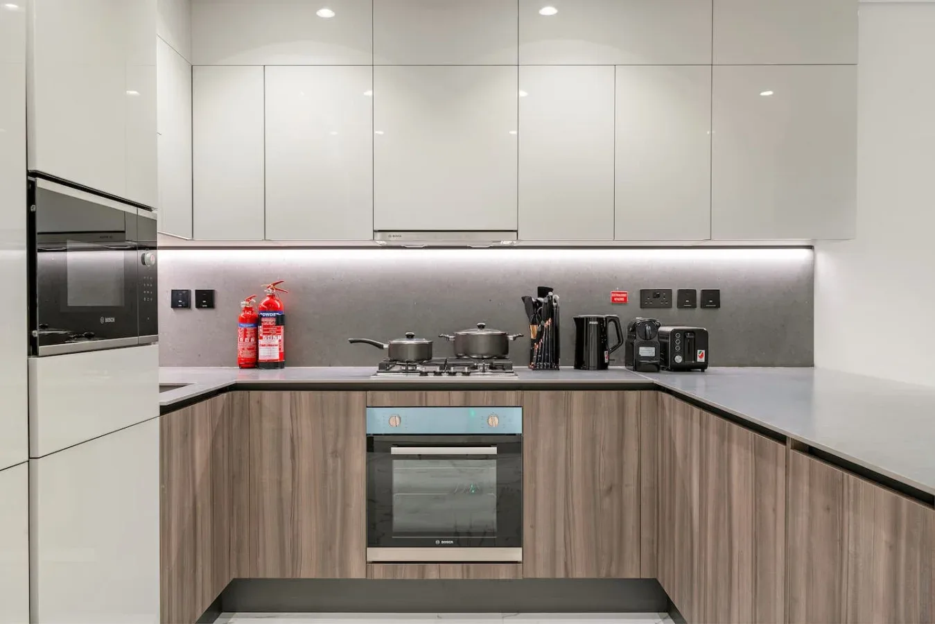 Una cocina moderna con armarios blancos, gabinetes inferiores de tono madera y electrodomésticos integrados.