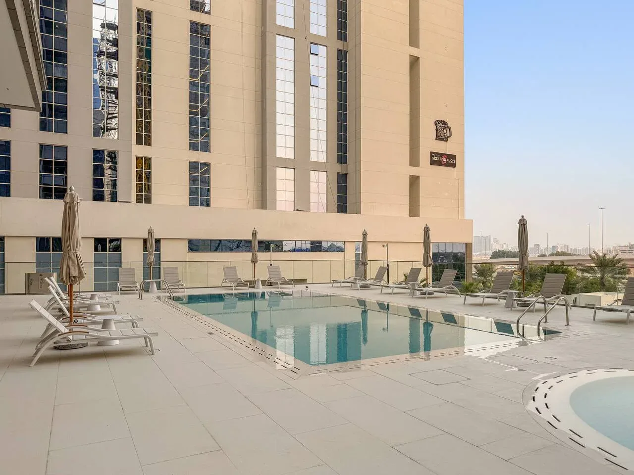 Una piscina al aire libre junto a un edificio alto, con asientos alrededor de la terraza.